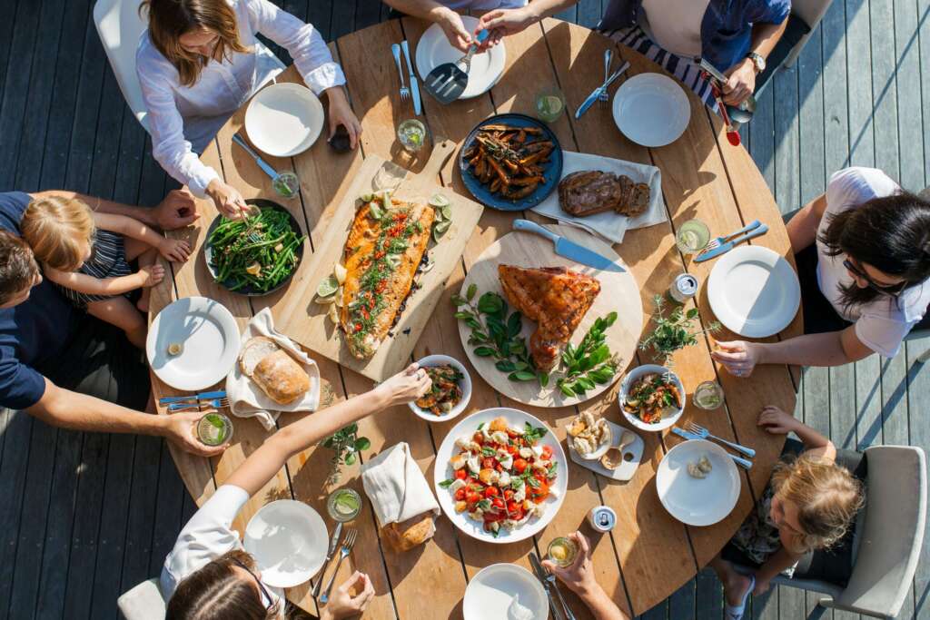 People enjoying a meal at a wooden table filled with various dishes outdoors