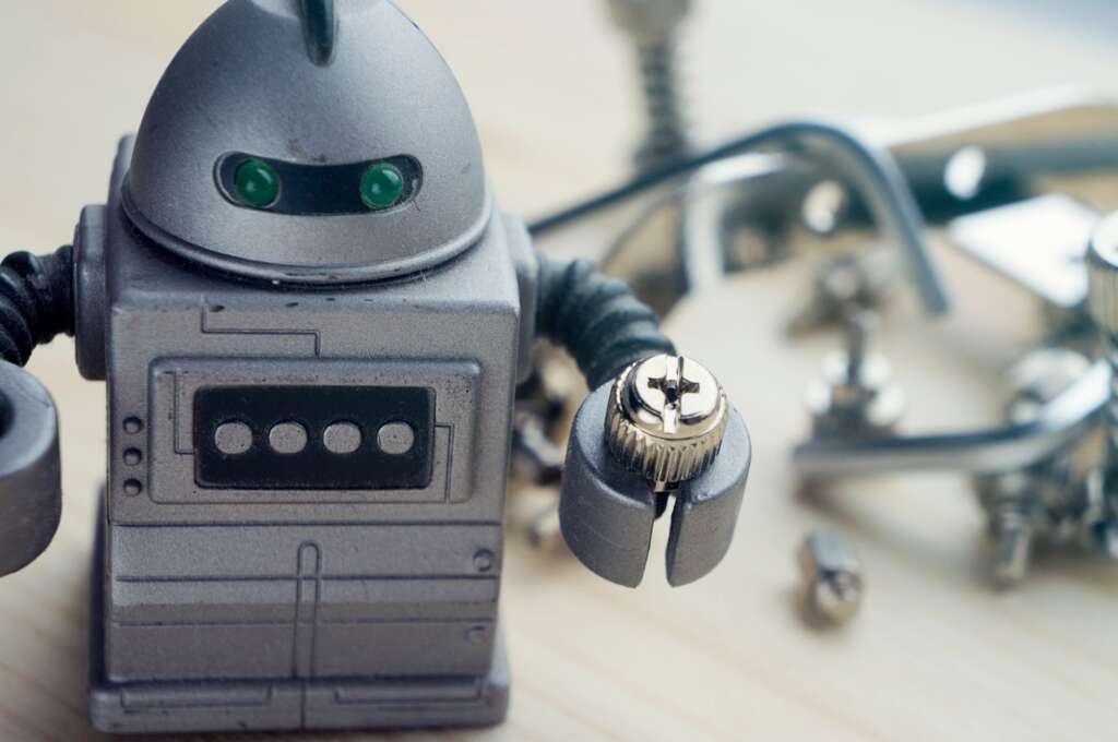 Gray robotic figure with green eyes in a hardware workshop.