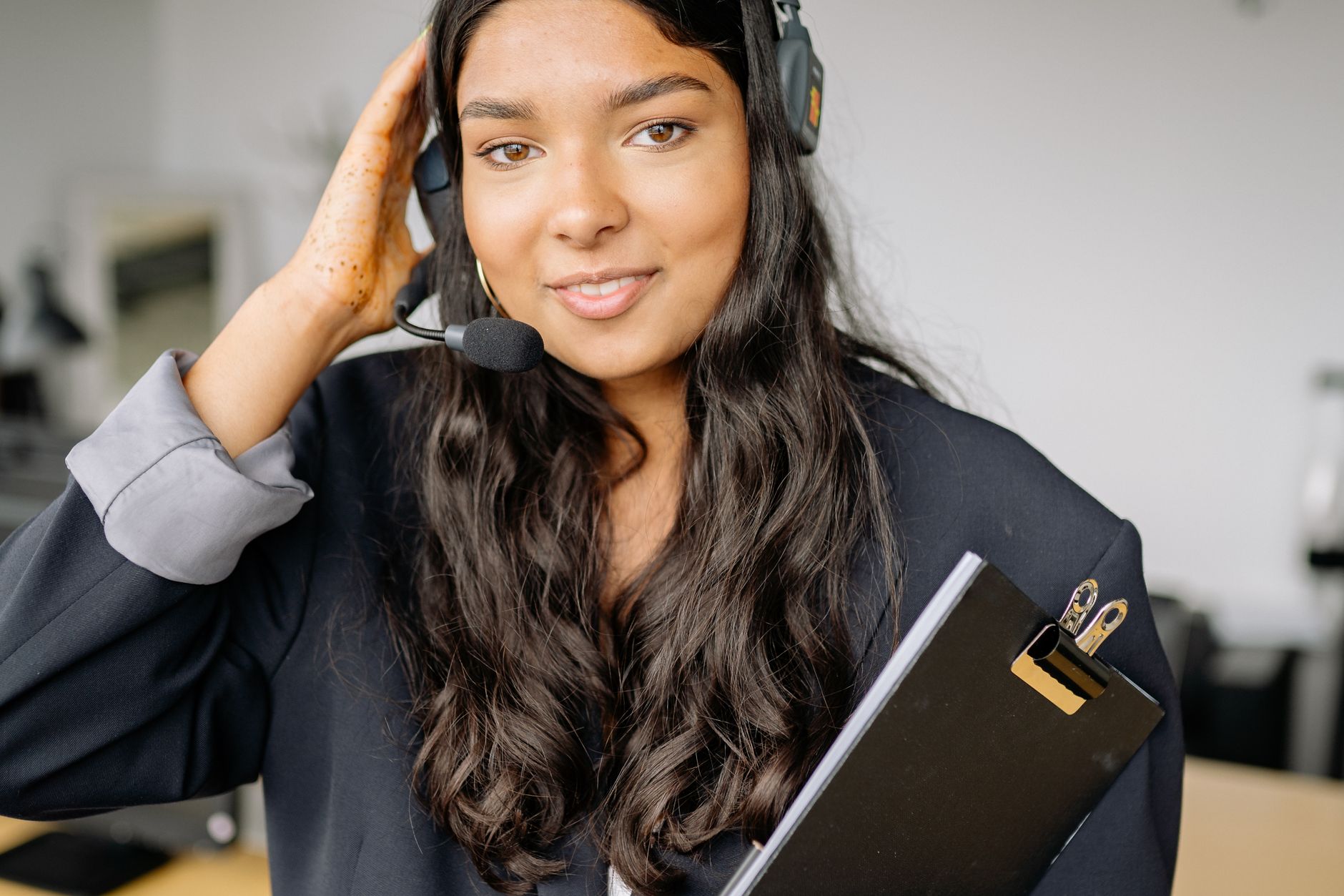 Young woman wearing a black headset at an office desk with a clipboard, focused on her work.