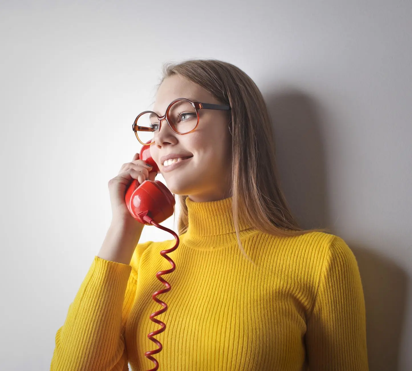 Young woman in yellow top and black sweater smiling on a phone call